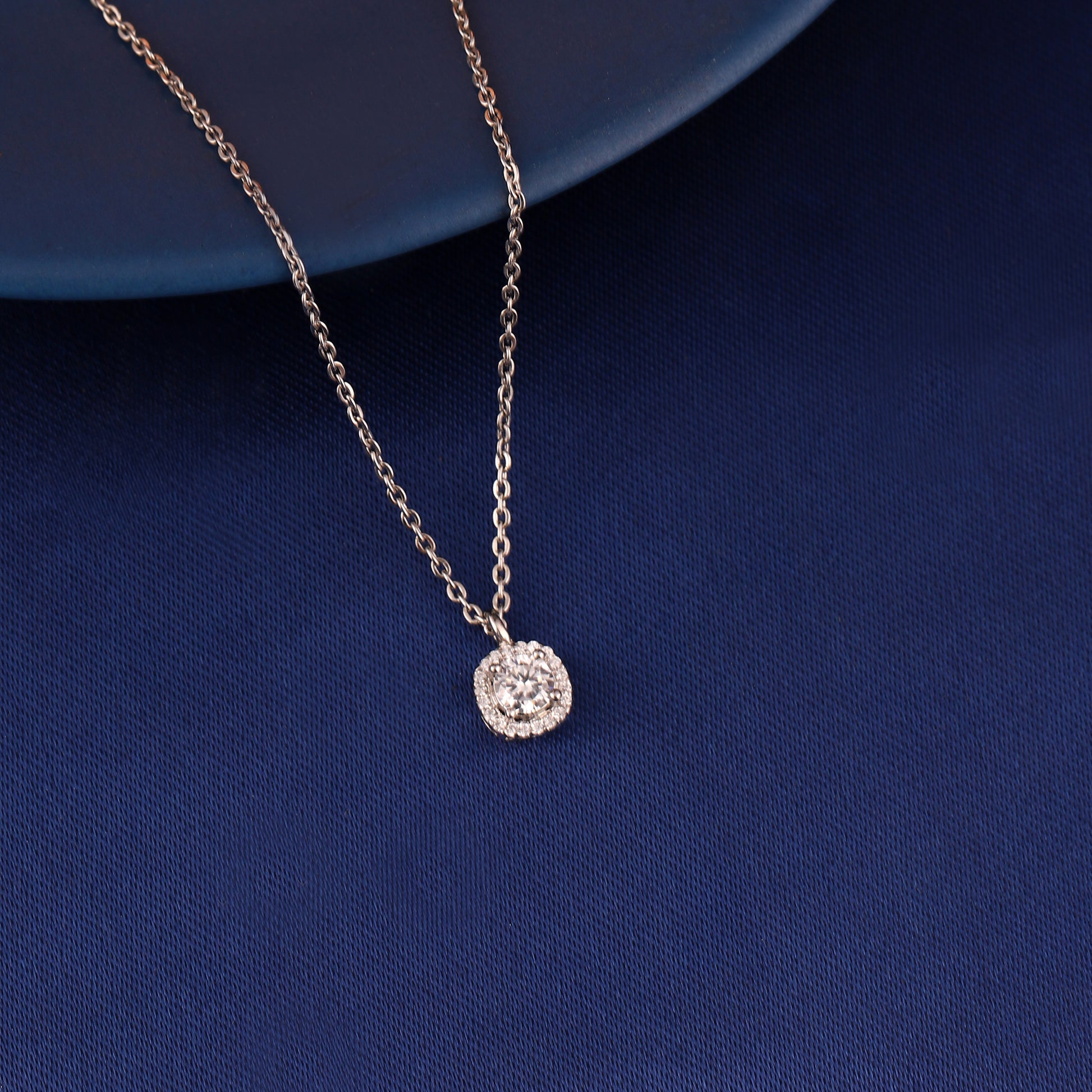 Cushion halo pendant necklace in 925 silver displayed on blue fabric background